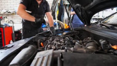 Araç kaputunun altında çalışan genç bir tamirci. Profesyonel oto tamircisi atölyedeki tornavida aletini kullanarak arabanın motorunu tamir eder. Erkek tamirci garajdaki otomobil motorunu kontrol ediyor. Yavaş çekim.