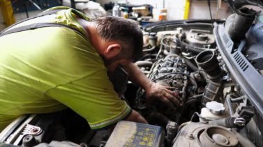 Yetişkin oto tamircisi atölyede arabanın bakımını yapıyor. Garajda kaputun altında çalışan profesyonel bir tamirci. Erkek tamirci iş yerinde otomobil motorunu kontrol ediyor. Aktarım tanısı.