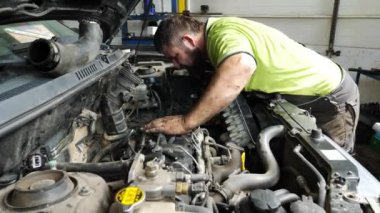 Atölyede kaputun altında çalışan üniformalı profesyonel bir tamirci. Mutlu tamirci kameraya bakıyor ve araba bakımından sonra baş parmağını kaldırıyor. Otomobil tanılama kavramı.