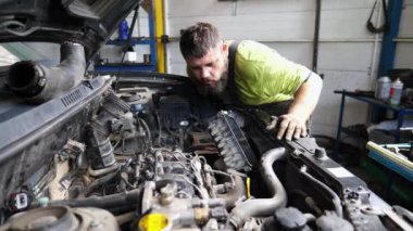Araba motorunu kontrol eden profesyonel bir tamirci. Garajda kaputun altında çalışan yetişkin oto tamircisi. Erkek tamirci atölyede otomobil motorunu kontrol ediyor. Taşıma bakımı.