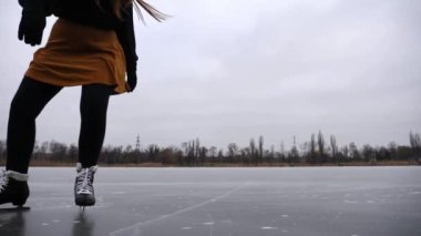 Genç kız donmuş nehirde rotasyon eğitimi alıyor. Buz pateni pistinde kayan artistik patenli bir kadın. Sporcu kadın soğuk havada gölette paten kayıyor. Kış günü boş vakit. Yavaş çekim.