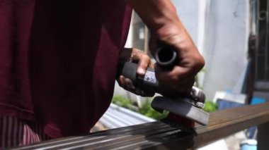 Profesyonel tamircinin erkek elleri özel bir enstrüman tutuyor ve paslı havadan metal yapısını temizliyor. Genç işçilerin kolları demir parçalarını elektrikli testere ile öğütüyor. Kapat..