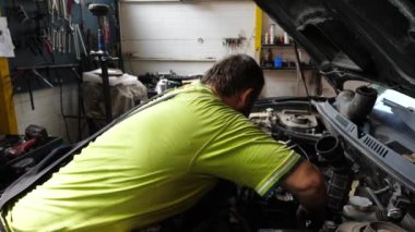 Yetişkin oto tamircisi atölyede arabanın bakımını yapıyor. Garajda kaputun altında çalışan profesyonel bir tamirci. Erkek tamirci iş yerinde otomobil motorunu kontrol ediyor. Aktarım tanısı.