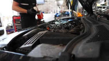 Genç oto tamircisi atölyedeki araca yeni yağ filtresi takıyor. Servis kaputunun altında çalışan profesyonel bir tamirci. Erkek tamirci iş yerinde ulaşımı tamir ediyor. Otomobil bakımı.