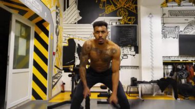 Dövüş halatlarıyla antrenman yapan güçlü Afrikalı sporcu fitness merkezinde. Modern spor salonunda sıkı çalışan kaslı Afro-Amerikan sporcusu. Sağlıklı ve aktif yaşam tarzı kavramı. Yavaş çekim.