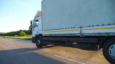 Kargo karavanıyla otoyolda gidip malları taşıyan kamyoneti kapatın. Beyaz kamyon gün batımında kırsal yolda hızla ilerliyor. Kargo taşıma konsepti. Yavaş çekim kenar görünümü.