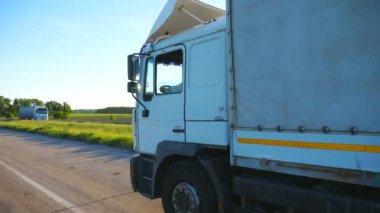 Kargo karavanı olan bir kamyonun yan görüntüsü otobanda gidiyor ve akşamları mal taşıyor. Kamyon kırsal yoldan geçerek hedefe gidiyor. Kargo taşıma konsepti. Yavaş çekim. Yakın çekim..