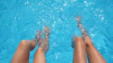 Kadın bacaklarının manzarası otel havuzunda berrak su sıçratıyor. Havzanın kenarında oturan iki arkadaş güneşli bir günde tatilin tadını çıkarıyorlar. Yaz tatili ya da tatil kavramı. Yavaş çekim.