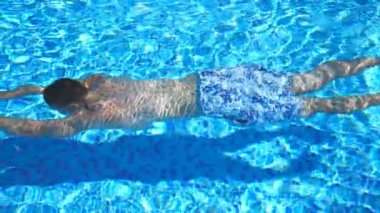 Otel havuzunda suyun altında yüzen şortlu tanınmaz bir adam. Yaz tatilinde otel havzasında yüzen adam. Güneşli bir günde yüzme havuzunda ferahlatıcı bir adam. Yavaş çekim. Yakın çekim..