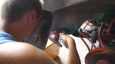 Erkek tamirci ya da tamirci eski arabanın metal parçalarını kaynaklama makinesiyle garajda kaynak yapıyor. Yetişkin kaynakçı atölyede profesyonel ekipman ve koruyucu maske kullanarak kaynakçılık yapıyor. Dolly vurdu..