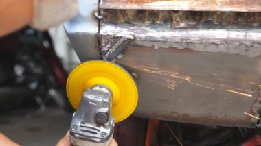 Erkek kaynakçı, atölyede öğütücü ve koruyucu gözlük kullanarak eski araba gövdesini öğütüyor. Garajda elektrikli aletlerle araba cilalayan bir tamirci ya da tamirci. Arka görünüm.