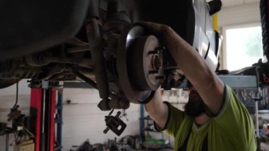 Üniformalı araba tamircisi atölyedeki ingiliz anahtarı aletini kullanarak arabanın tamirini yapıyor. Profesyonel erkek tamirci garajdaki bir kaldırma aracının altında çalışıyor. Otomobil bakımı kavramı.