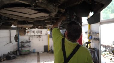 Erkek oto tamircisi atölyede kaldırma aracının altında çalışıyor. Yetişkin profesyonel tamirci serviste ya da garajda araba tamir ediyor. Düzenli otomobil bakımı kavramı. Yavaşça kapat..