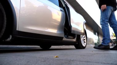Erkek el elektrikli SUV arabasının arka kapısını açıyor. Elektrikli otomobilin kapısını açmak için düğmeye basan adam. Adam modern otomatiğe oturuyor. Çağdaş teknolojiler kavramı.