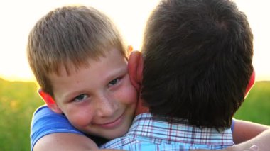 Kırsal kesimde küçük mutlu oğlunun elini tutan genç bir baba. Küçük gülümseyen çocuk kameraya bakıyor ve arka planda parlak güneş ışığına karşı babasına sarılıyor. Aile dinlenmesi kavramı. Kapat..