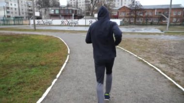 Atletik sporcu, bulutlu bir günde okul stadyumunda koşuyor. Genç sporcu atletizm sahasında koşuyor. Spor giyim bölümünde dışarıda egzersiz yapan güçlü bir adam. Aktif sağlıklı yaşam tarzı.