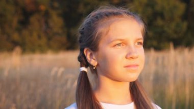 Güzel bayan çocuk portresi çim tarlasında duruyor ve sarı saçlarıyla oynuyor. Parlak güneş ışınlarıyla aydınlatan küçük tatlı bir kız yüzü. Mutlu küçük çocuk doğada dinleniyor. Dolly vurdu..