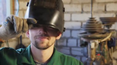 Gülümseyen genç tamirci işini bitirdikten sonra koruyucu maskeyi açar. Üniformalı tamircinin portresi gülüyor ve kameraya bakıyor. Seminerde çalışan sakallı mutlu kaynakçı. Yavaşla..