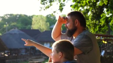 Babası ve oğlu kırsalda birlikte vakit geçiriyorlar. Küçük çocuk kırsal kesimde babasına bir şey gösteriyor. Güneşli yaz gününde doğada dinlenen mutlu bir aile. Yavaşça kapat..