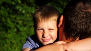 Küçük oğlunun elini tutan ve kırsalda yürüyen genç bir baba. Küçük çocuk kameraya bakıyor ve babasına sarılıyor. Güneşin parlak ışıklarıyla aydınlatan sevimli gülümseyen çocuğun yüzü.