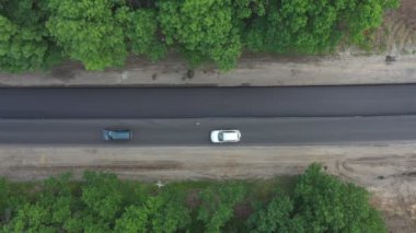 Ormandan geçen yeni asfalt yolunun hava görüntüsü. Açığa çıkan otoyolda giden arabaların üst görüntüsü. Otomobiller yol çalışmasından sonra kırsal otoyolda sürüyorlar. Araç trafiği.