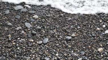 Güneşli bir günde küçük dalgalar çakıl taşı plajına vuruyor. Okyanus gelgitleri taşlı kıyıları silip süpürüyor. Parlak güneş ışığından parlayan ıslak taşlar. Güzel deniz manzarası. Seyahat konsepti. Yavaş çekim. Yakın çekim..