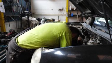 Yetişkin oto tamircisi atölyede arabanın bakımını yapıyor. Garajda kaputun altında çalışan profesyonel bir tamirci. Erkek tamirci iş yerinde otomobil motorunu kontrol ediyor. Aktarım tanısı.
