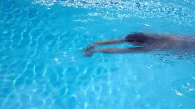 Saydam berrak suyla havuzda yüzen tanınmayan bir kadın. Genç kız yaz tatilinde otel havzasında yüzüyor. Yaz tatili kavramı. Yavaş çekim kenar görünümü