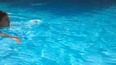 Sıcak bir yaz gününde havuzda mavi berrak suyla yüzen çekici bir kadın profili. Genç kız havuzda dinlenirken dinleniyor. Tatil sırasında bir bayan. Ağır çekim. Yaklaş..