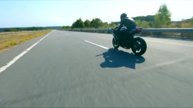 Anayolda motosiklet süren motosikletliyi takip edin. Motosikletli, kır yolunda motosikletiyle yarışıyor. Yolculuk sırasında bisiklet süren adam. Yolculukta özgürlük ve macera kavramı. Hava görüntüsü.