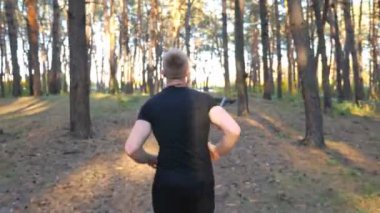 Güneşli bir günde orman yolunda koşan tanınmayan bir adam. Erkek sporcu, dışarıda çalışıyor. Atletik adam kardiyo antrenmanı yapıyor. Tahtada koşuyor. Sağlıklı aktif yaşam tarzı kavramı. Yavaş çekim