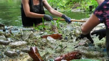 Koruyucu eldivenli kadın çevrecilerin elleri enkaz nehirlerini temizliyor. Kirli gölde plastik şişe toplayan kauçuk elbiseli tanınmayan gönüllüler. Çevre kirliliği koruması.