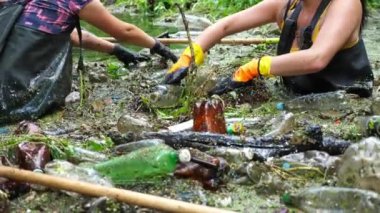 Koruyucu eldivenli kadın çevrecilerin elleri enkaz nehirlerini temizliyor. Kirli gölde plastik şişe toplayan kauçuk elbiseli tanınmayan gönüllüler. Çevre kirliliği koruması.