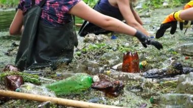 Koruyucu eldivenli kadın çevrecilerin elleri enkaz nehirlerini temizliyor. Kirli gölde plastik şişe toplayan kauçuk elbiseli tanınmayan gönüllüler. Çevre kirliliği koruması.