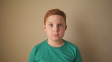 Çilli, mutlu, kızıl saçlı çocuk kameraya bakıyor ve el kaldırıyor. İçerideki başarısını alkışlıyor. Yüzünde olumlu duygular olan kızıl erkek çocuk portresi. Yavaş çekim.