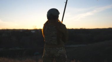 Girl in military uniform and helmet waving flag of Ukraine against sunset background. Female ukrainian army soldier lifted up yellow-blue flag. Victory against russian aggression. Invasion resistance.
