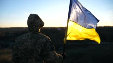 Ukrayna bayrağı sallayan tanınmamış Ukraynalı asker. Askeri üniformalı adam gün batımına karşı bayrak kaldırdı. Rus saldırısına karşı zafer. İstila direnci konsepti. Yavaş çekim.