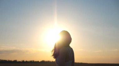 Kadın silueti buğday tarlalarının arasında duruyor ve güzel yaz günbatımını seyrediyor. Akşamları özgürlüğün ya da dışarıda eğlenmenin tadını çıkaran çekici mutlu bir kız. Doğayla uyum. Yavaş çekim.