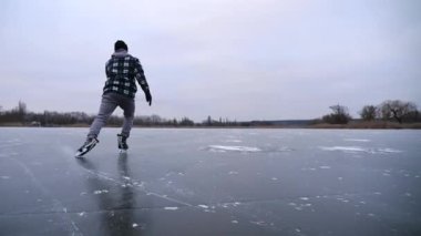 Erkek kaykaycı bulutlu kış gününde donmuş nehirde kayıyor. Genç adam buz pateni pistinde buz pateni yaparken nallandı. Soğuk havada gölde sporcu eğitimi. Kış zamanı aktif bir eğlence. Yavaş çekim