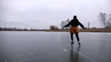 Bulutlu bir günde buz yüzeyinde buz pateni yapan kadın patenci. Sporcu kadın, donmuş nehir ya da gölde artistik patinaj eğitimi almış. Kadın becerilerini geliştiriyor ve kış soğuğunda aktif boş vakitleri oluyor. Yavaş çekim