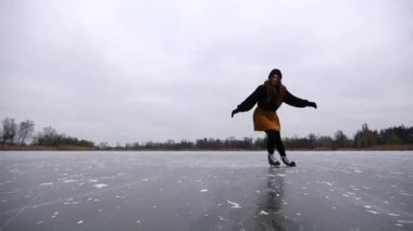 Dışarıdaki buz patenleriyle kayan genç bir kadın. Sporcu kadın donmuş nehirde ya da gölde kayıyor. Kız spordan hoşlanıyor ve soğuk kış havasında aktif boş vakit geçiriyor. Yavaşça kapat..