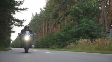 Kırsal sokakta motosiklet süren kasklı bir adam. Ormanın yakınındaki kır yolunda motosikletini süren bir motosikletli. Yolculuk sırasında bisiklet süren adam. Özgürlük yaşam tarzı ve macera kavramı. Yavaş çekim.