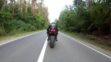 Orman yolundaki motosikletli motorcuları takip edin. Kasklı adam ormanın yakınındaki kırsal yolda modern spor motosiklet yarışı yapıyor. Yolculuk sırasında ya da yolculukta bisiklet süren adam. Özgürlük kavramı.