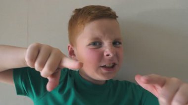 Sevimli yakışıklı bebek seviniyor ve kamerayı işaret ediyor. Kapalı alanda çilleri olan mutlu kızıl saçlı çocuğun portresi. Yüzünde neşe ifadesi olan erkek çocuğun duygularını kapat. Yavaş çekim.