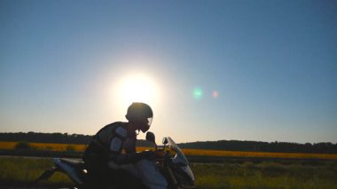 Adam bir motosiklet sürme. Onun motosiklet sürüş ülke yolda günbatımı sırasında motosikletçi. Ağır çekim yan Görünümü Kapat.