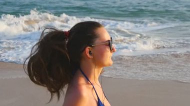 Deniz plajında çalışan mayo ve müzik dinleme genç kadın. Okyanus kıyısında kız jogging. Kadın Sporcusu açık egzersiz. Doğada sağlıklı aktif egzersiz yaşam tarzı. Yakın çekim yavaş hareket.
