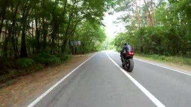 Orman yolundaki motosikletli motorcuları takip edin. Kasklı adam ormanın yakınındaki kırsal yolda modern spor motosiklet yarışı yapıyor. Yolculuk sırasında ya da yolculukta bisiklet süren adam. Özgürlük kavramı.