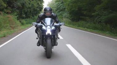 Kırsal Orman Yolu 'nda modern spor motosiklet süren kasklı genç bir adam. Motosikletli, tahta yolda motosikletiyle yarışıyor. Yolculuk sırasında bisiklet süren adam. Özgürlük ve macera kavramı. Ön görünüm.