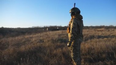 Kamuflaj üniformalı genç askerler gün batımına karşı ellerinde Ukrayna bayrağıyla çayırda duruyorlar. Ukrayna ordusundan bir çift, savaş alanında el ele tutuşan bayrağı kaldırdı. Dolly vurdu..