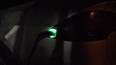 Elektrikli araba akşam şarj oluyor. Güç konnektörü EV otomobiline yerleştirildi. E-araç aküsünün şarj işlemi. Çevre dostu sıfır emisyon otomatiği. Temiz enerji doldurma teknolojisi.